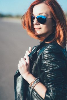 red-haired girl in a black jacket and blue glasses on a gray road