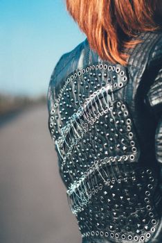 red-haired girl in a black jacket and blue glasses on a gray road