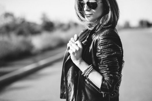 red-haired girl in a black jacket and blue glasses on a gray road