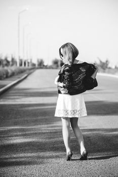 red-haired girl in a black jacket and blue glasses on a gray road