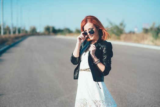 red-haired girl in a black jacket and blue glasses on a gray road