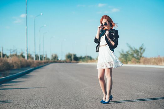 red-haired girl in a black jacket and blue glasses on a gray road