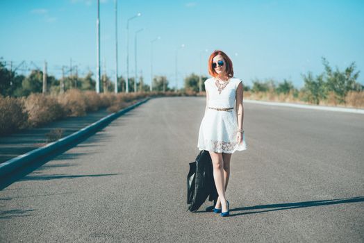 red-haired girl in a black jacket and blue glasses on a gray road