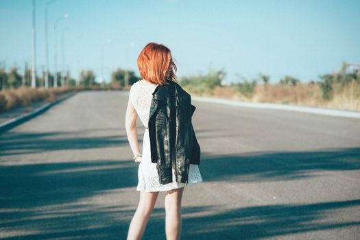red-haired girl in a black jacket and blue glasses on a gray road