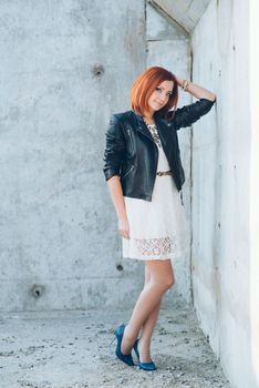 red-haired girl in a black jacket and blue glasses on a gray road