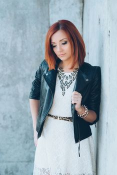 red-haired girl in a black jacket and blue glasses on a gray road