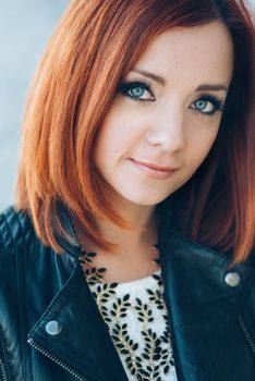 red-haired girl in a black jacket and blue glasses on a gray road