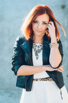 red-haired girl in a black jacket and blue glasses on a gray road