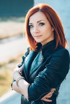 red-haired girl in a black jacket and blue glasses on a gray road