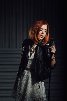 young red-haired girl in a white dress and a black leather rocker jacket sings emotionally into the microphone