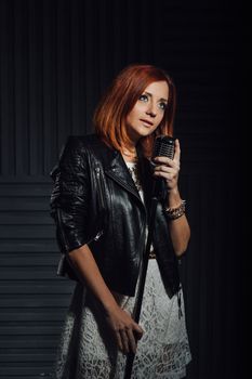 young red-haired girl in a white dress and a black leather rocker jacket sings emotionally into the microphone