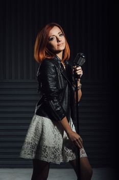 young red-haired girl in a white dress and a black leather rocker jacket sings emotionally into the microphone