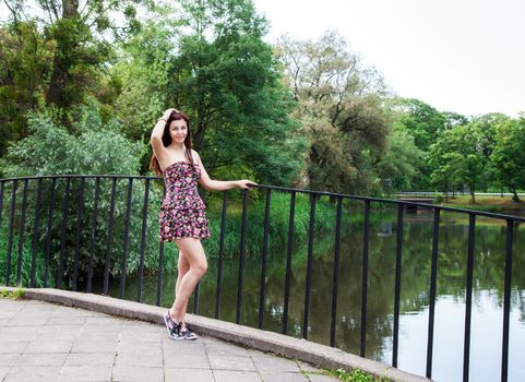 young beautiful brunette standing on the bridge near the river on summer day