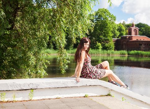 young beautiful brunette sitting near the lake on sunny summer day