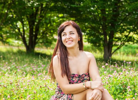 young beautiful smiling girl sitting on the grass outside on sunny summer day