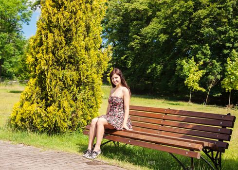 young beautiful smiling woman girl sitting on a park bench on sunny summer day
