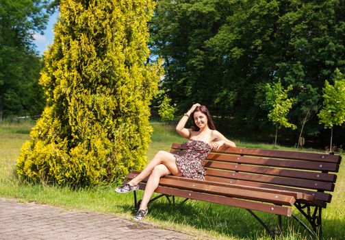 young beautiful smiling girl girl sitting on a park bench on summer day