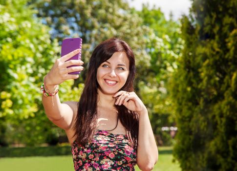 young beautiful girl doing selfie mobile phone in the park on summer day