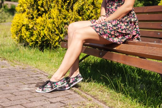 young woman sitting on a park bench on sunny summer day. legs closeup