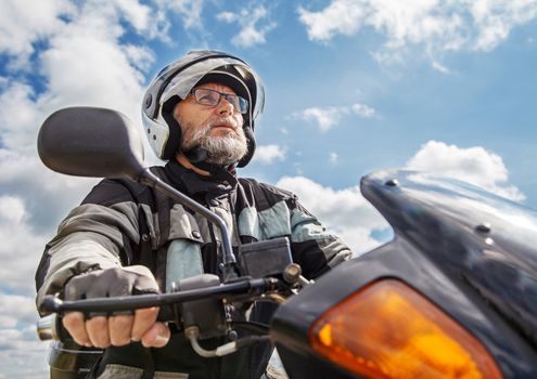 elderly motorcyclist wearing a jacket and glasses with a helmet sitting on his motorcycle on the road closeup