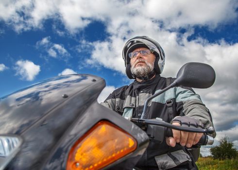 elderly motorcyclist wearing a jacket and glasses with a helmet sitting on his motorcycle on the road closeup