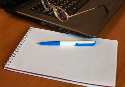 pen with notebook and glasses near laptop on the table