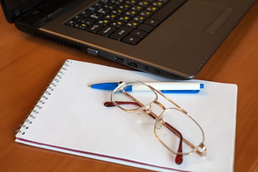 glasses with notebook and pen near laptop on the table