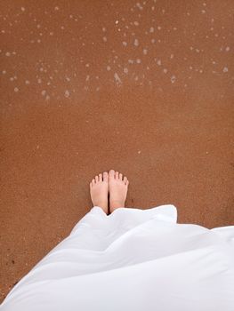 Legs of a girl in a white dress by the sea wave on the shore.