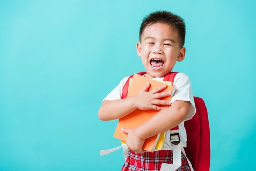 Back to school concept. Portrait Asian happy funny cute little child boy smiling and laugh hug books, studio shot isolated blue background. Kid from preschool kindergarten with school bag education