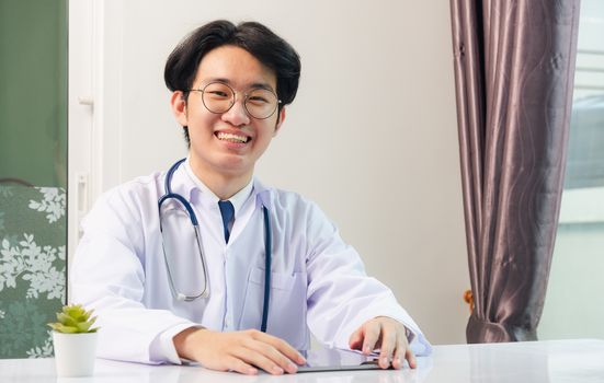 Happy Asian young doctor handsome man smile work from home office wear glasses, using black modern smart digital tablet computer on desk at hospital office, Technology healthcare and medicine concept