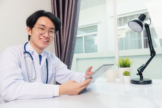 Happy Asian young doctor handsome man smile work from home office wear glasses, using black modern smart digital tablet computer on desk at hospital office, Technology healthcare and medicine concept