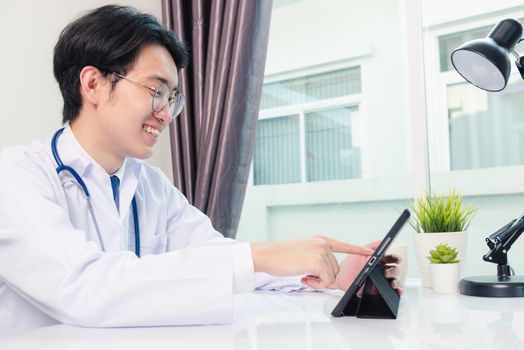 Happy Asian young doctor handsome man smile work from home office wear glasses, using black modern smart digital tablet computer on desk at hospital office, Technology healthcare and medicine concept