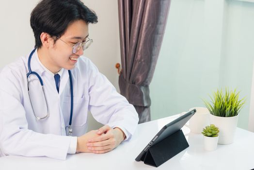 Happy Asian young doctor handsome man smile wear glasses use modern smart digital tablet computer sit and listen patient explain symptoms on desk at hospital office, Technology Healthcare And Medicine