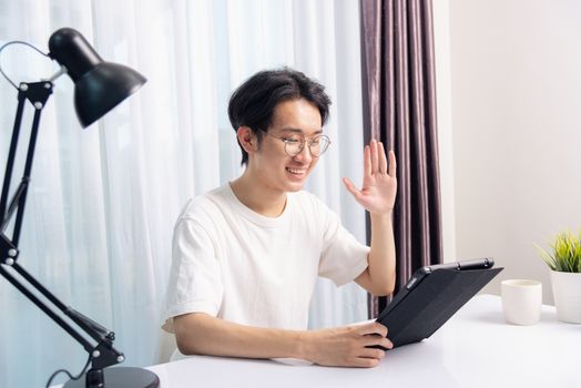 Happy Asian young business handsome man work from home office wear glasses, t-shirt comfortable he smiling and using a black modern smart digital tablet computer to read email or learning on desk