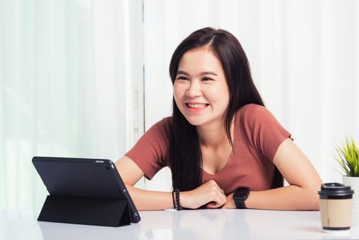 Work from home, Asian business young beautiful woman smiling sitting on desk workspace talking communicating with team video chat or conferencing on digital tablet computer at home office
