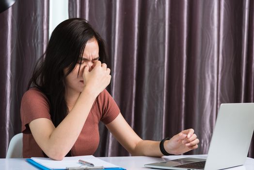 Work from home, Fatigued or strain Asian business young beautiful woman sits on desk workspace feeling tired stressed hold his nose close eyes after see screen long time of laptop computer at office