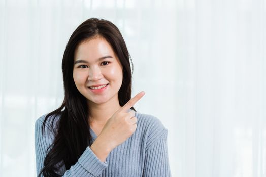 Close up headshot portrait young Asian happy beautiful woman healthy smiling face long hair stand pointing finger to side away space, studio shot looking to camera at home and have a copy space