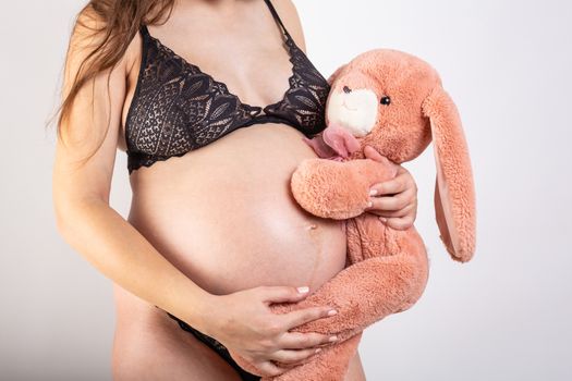 Close-up pregnant woman's belly with Hare toy. Beautiful pregnant woman. Pregnancy, parenthood, preparation and expectation concept