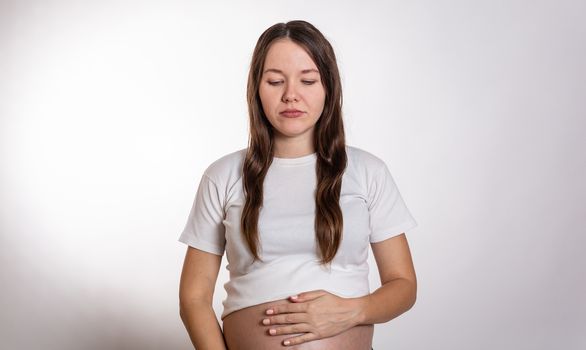 The young beautiful pregnant woman experiences strong emotions on a white background.