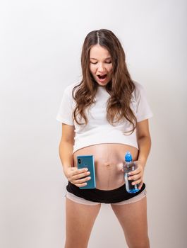 beautiful pregnant brunette woman drinking water from the bottle on isolated white background.