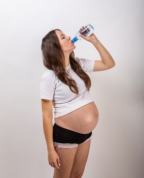 beautiful pregnant brunette woman drinking water from the bottle on isolated white background.