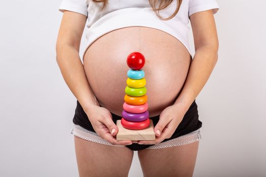 Pregnant girl with a wooden rainbow pyramid for children.