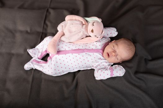 pretty smiling baby girl and toy rabbit lying in darck background.