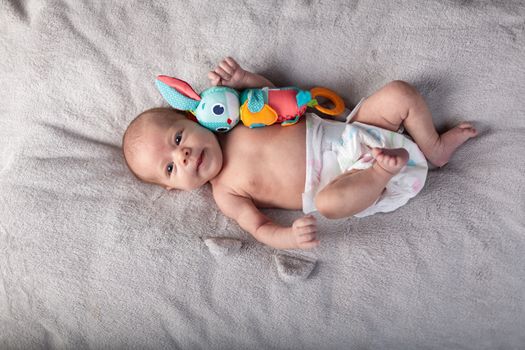 pretty smiling baby girl and toy rabbit lying in light background.