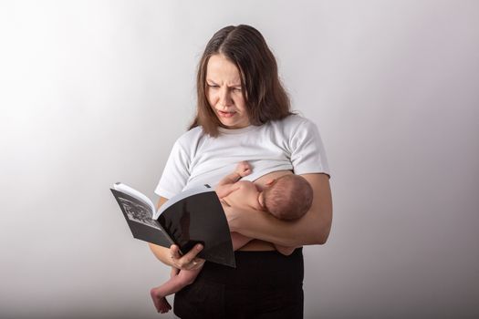 Beautiful young mother breastfeeding a baby while reading a black book.