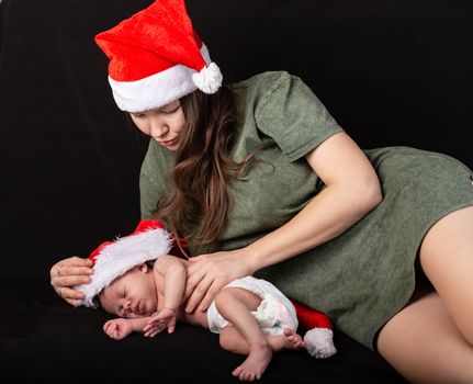 Mother and baby in santa red dress smile on a darck background.