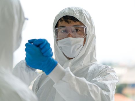 Epidemiological researchers in an anti-virus suit join hands to congratulate each other after the end of the experiment. Coronavirus disease 2019 testing process in a laboratory. 