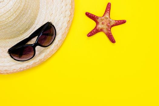 Summer holidays and vacation concept - sunglasses, starfish and a a retro beach straw on a yellow background with copy space.