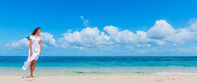 Woman in white dress walking on tropical beach, tropical sea on background