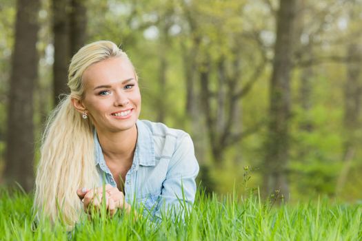 Happy smiling young woman laying on the green grass